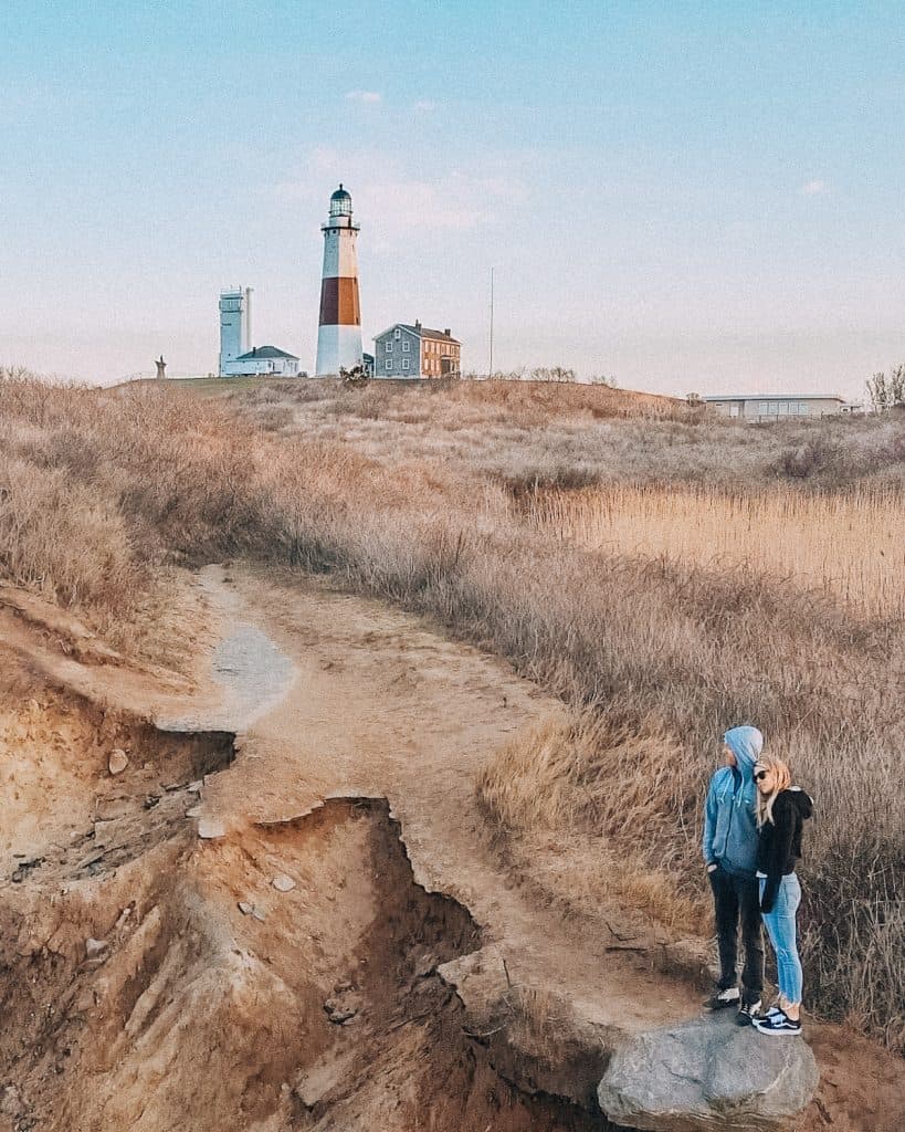 Montauk lighthouse on top of cliffs with two people standing below