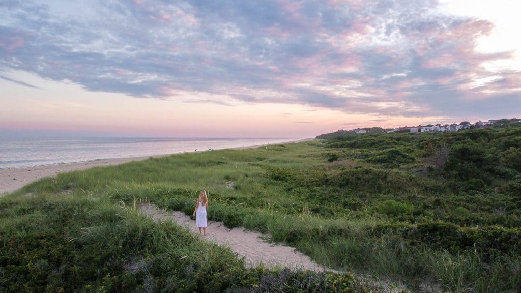 woman walking down sandy path towards beach and dunes in montauk ny