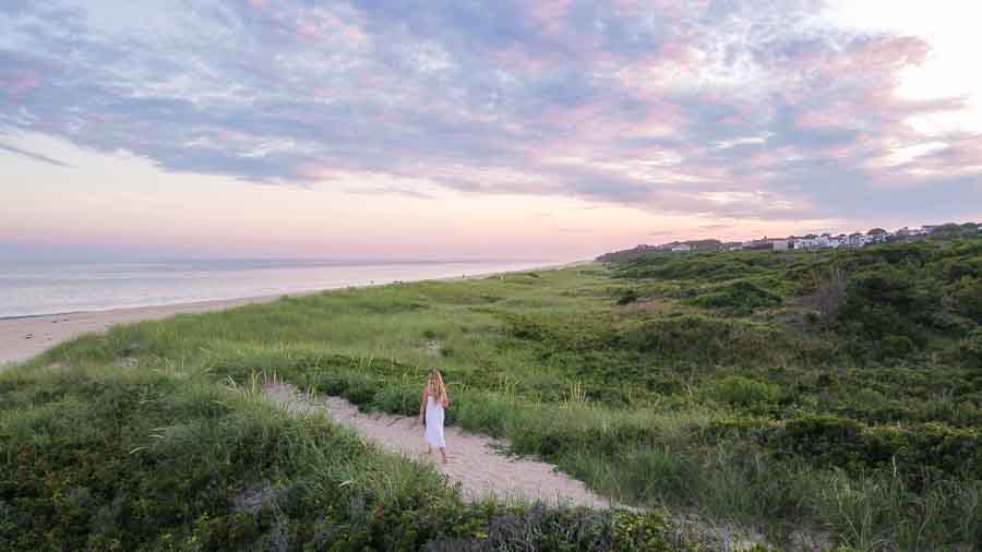 woman walking down sandy path to beach between dunes at sunset in Montauk NY