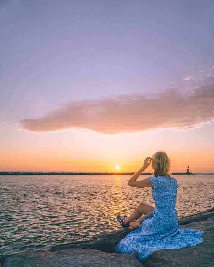 woman wearing blue dress sitting on jetty infront of sunset montauk ny
