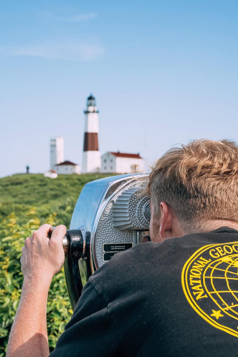 man in black shirt holding telescope pointed towards montauk lighthouse